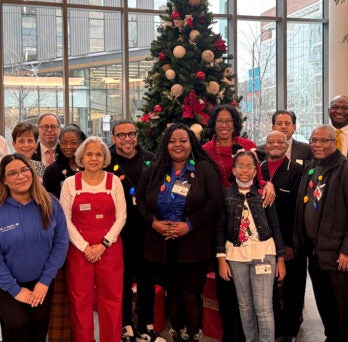 20 people posing together in the hospital atrium in front of a large festive Christmas tree 