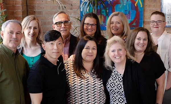 A group of 10 diverse individuals posing together in an office environment