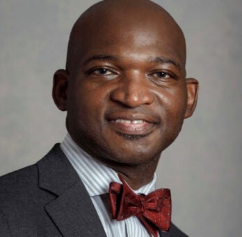 African American in a gray suit coat, striped shirt and maroon neck tie, smiling into the camera 