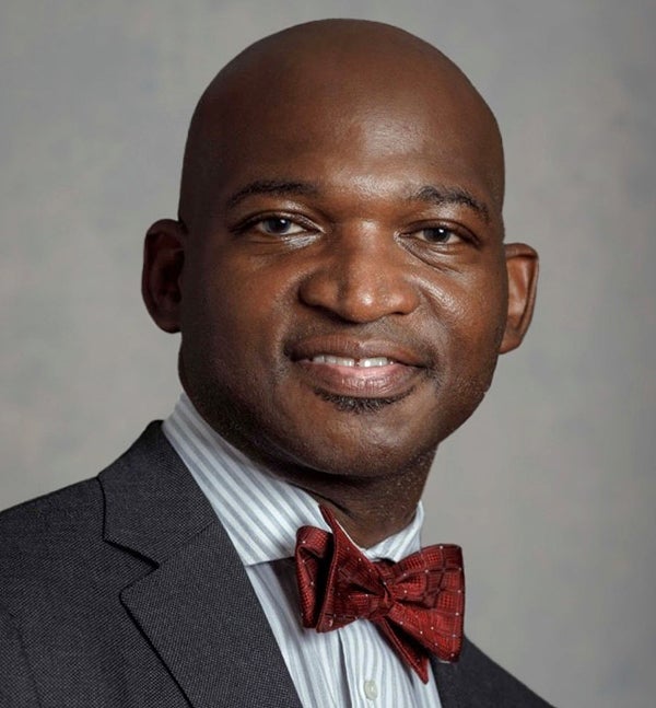 African American in a gray suit coat, striped shirt and maroon neck tie, smiling into the camera