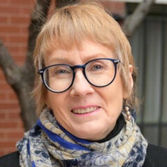 Woman with short reddish hair, wearing glasses and a scarf around her neck