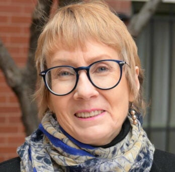 Woman with short reddish hair, wearing glasses and a scarf around her neck 