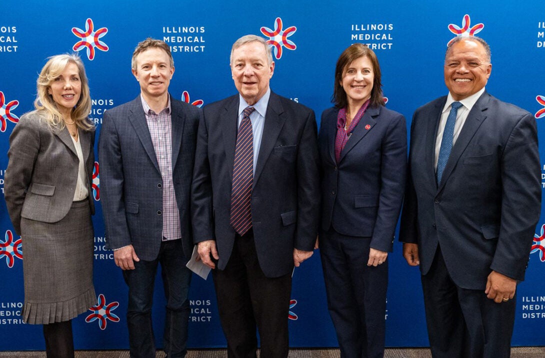 Five people in formal attire posing together in front of a backdrop with the Illinois Medical District logo
