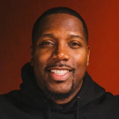 Man with short black hair, beard and mustache, wearing a black hoodie