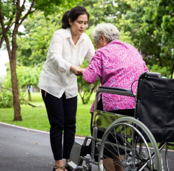 An elderly woman being helped up out of a wheelchair by a younger woman 