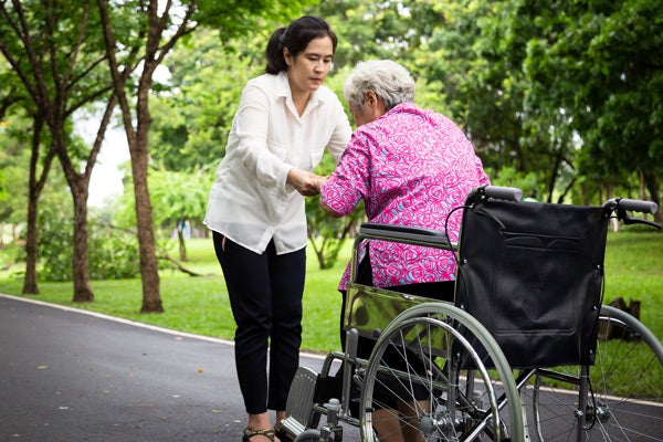 An elderly woman being helped up out of a wheelchair by a younger woman